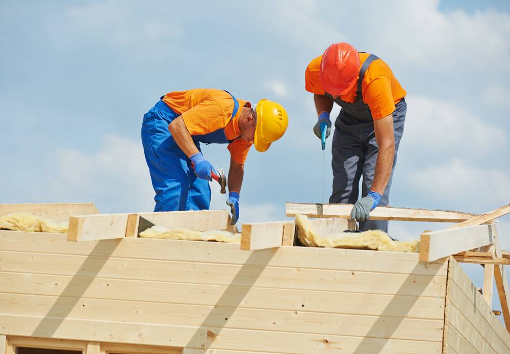 A view of 2 people working on the top of a wooden roof in orange uniform
